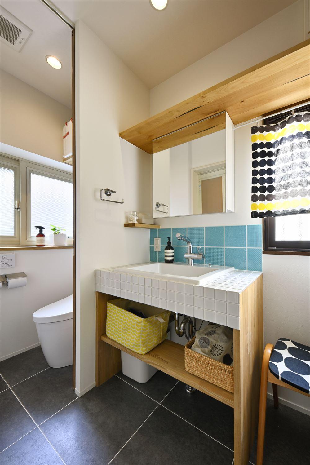 真っ白な角タイルを用いたシンプルな洗面台は造作。清潔感ある水色のタイルはキッチンと色違い。トイレは洗面室の奥に移動して水廻りを集約した