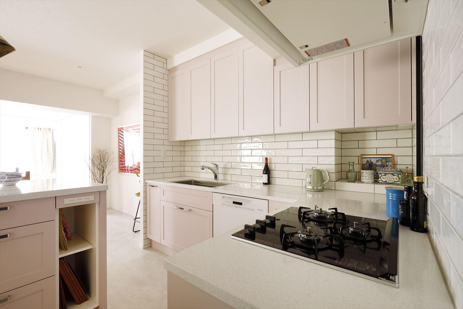 オーダーメイドキッチンを手がけるメーカーと入念な打ち合わせを重ねてイメージ通りに仕上げた。ベビーピンクの面材とピュアホワイトのタイルが印象的。アイランドのカウンターは収納を兼ねており、コンセントなど機能も充実している