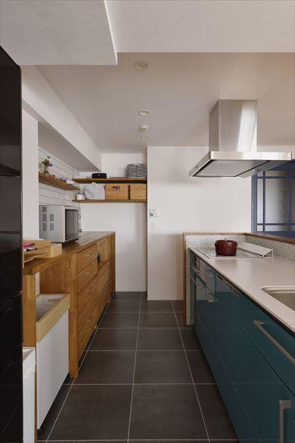 キッチンはご主人の提案でブルーをセレクト。カウンターの内側はモザイクタイルで可愛く彩った。キッチンの向き90度変えたのでダイニングスペースや正面の水廻りも行き来がしやすい。キッチンの収納は背面に集約。あらかじめサイズを測ってオープン棚を造作し既製品の収納をぴったり収めた