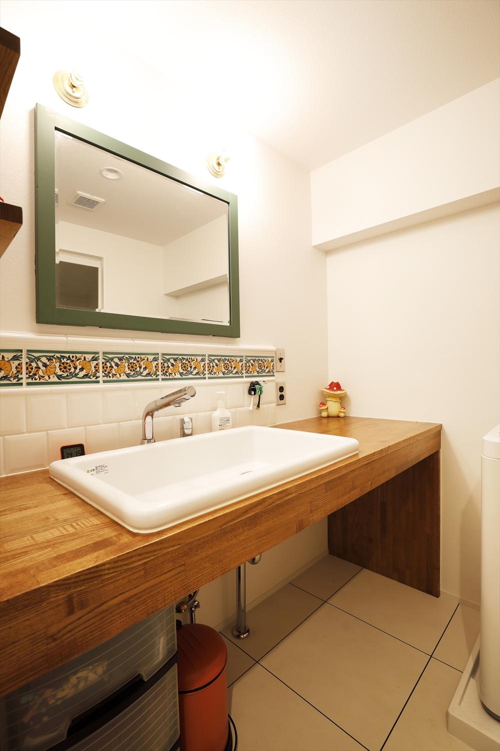 シンプルな洗面カウンターは造作。壁の花柄のタイルはNさんが気に入って購入したものを貼った。鏡は既存を再利用。フレームはタイルのグリーンに合わせて塗装して仕上げた。床はフロアタイルで掃除もしやすく。