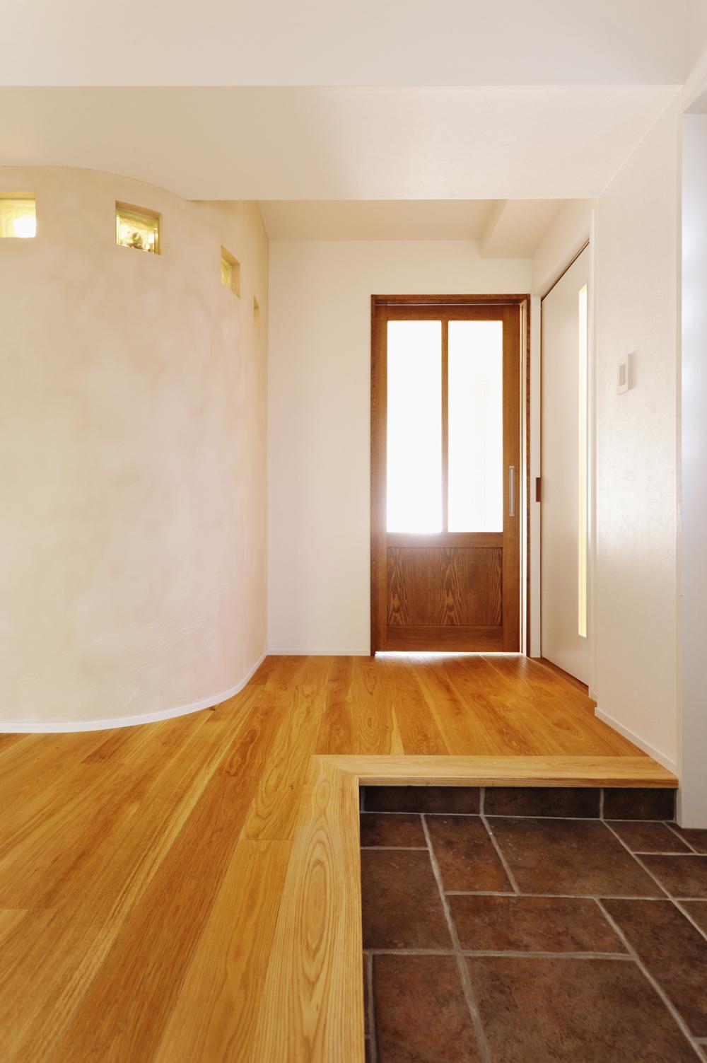 玄関入って右手を見たところ。丸い壁の向こうはキッチン奥のパントリー。丸い壁はスペースを取りつつ圧迫感の軽減と行き来のしやすい動線確保のための工夫。天井近くに配置されたガラスブロックからパントリーの光が柔らかく届く。