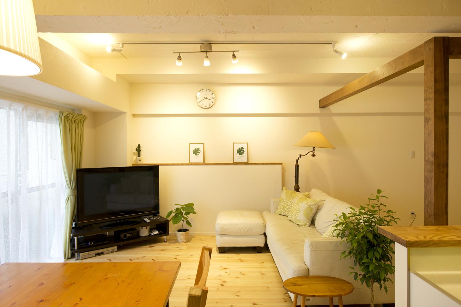 バルコニーからの光がたっぷり入る明るいリビング。床は明るい色合いのレッドパインの無垢材。テレビの後ろの壁は、以前キッチンがあった部分。躯体に埋め込まれていた元キッチンの配管を隠すため、腰壁の部分のみふかしてカウンターとして活用