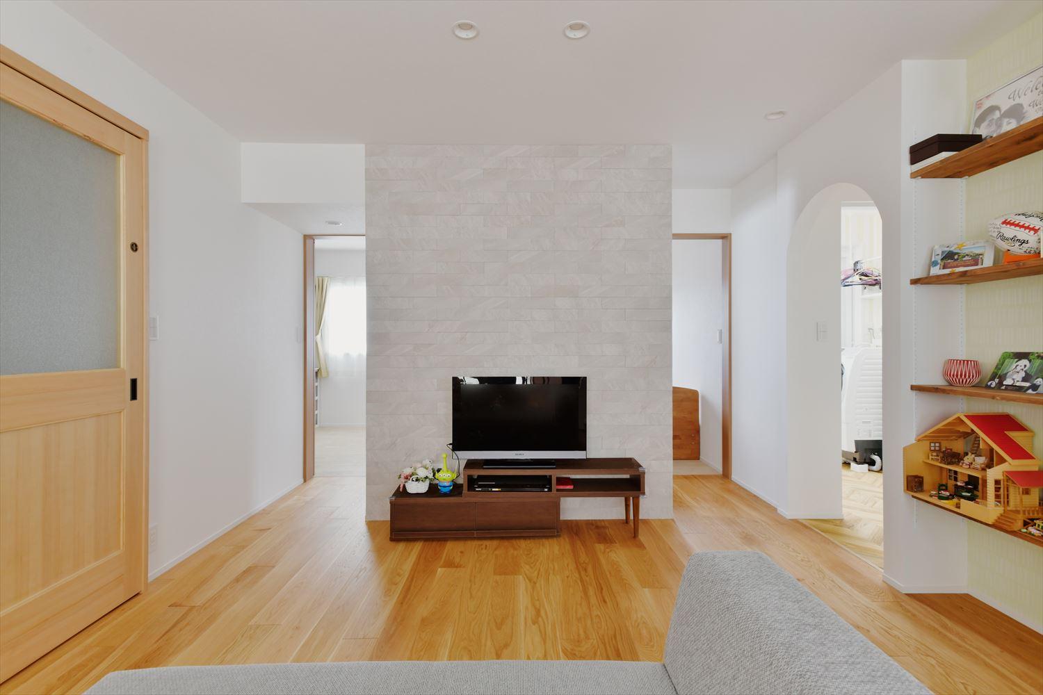 TV背面の壁には調湿効果のあるエコカラットを貼った。リビング空間全体の空気が心地いい。2つの部屋をつなげた居室には入り口を２つ設け、将来再び仕切れるように。壁面の収納は収納するものや量に応じて棚の位置を変えられるので便利