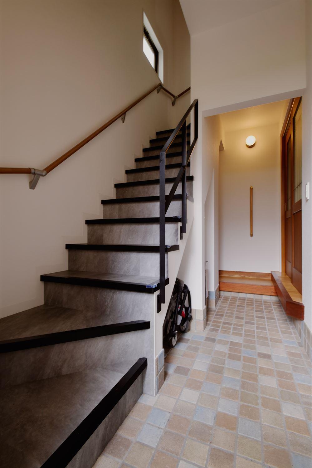 玄関土間を広げて、世帯を分ける階段を設置。靴のまま２階に上がれるよう、階段にはフロアタイルを貼った。階段の裏側はベビーカー置き場やアウトドアグッズの収納スペースとして活用できる。