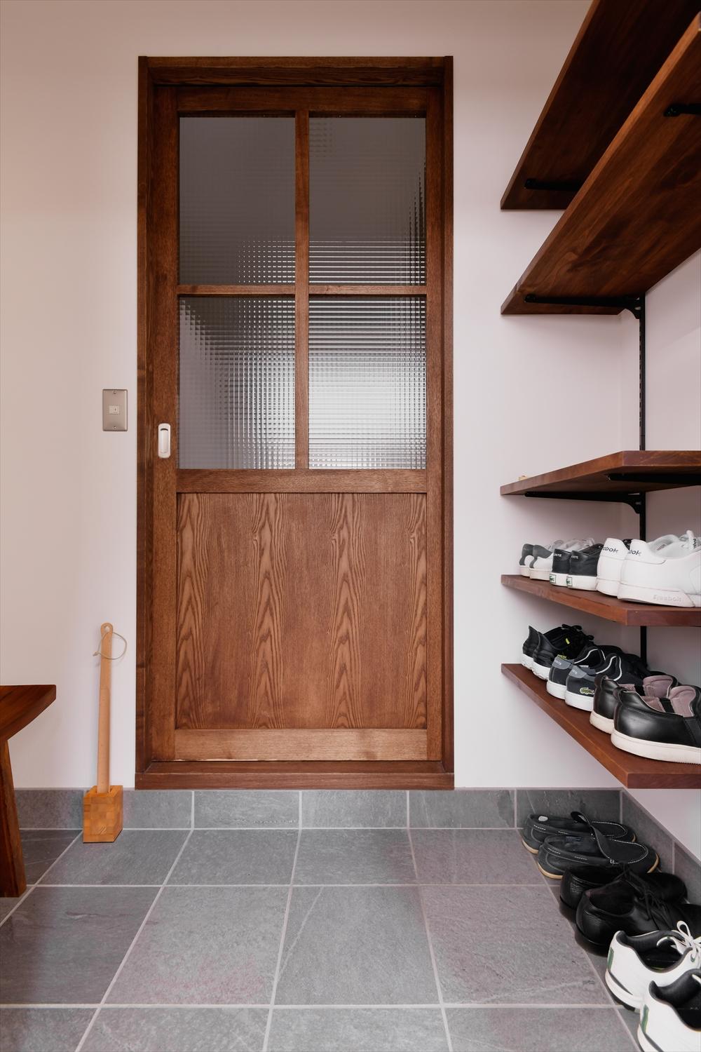 玄関土間は左手のスペースを拡大。右手にあったシューズボックスは撤去し、オープンな棚に。収納量と解放感を確保。ほぼワンルームで繋がる室内と玄関は大きなガラス入りの建具で仕切った。プライバシーを確保しつつ、玄関まで光が届いている。