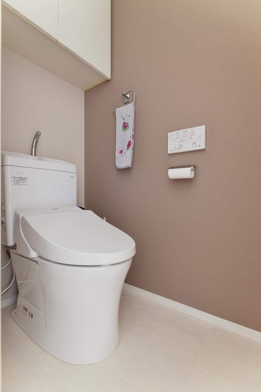 ベージュのクロスが優しい雰囲気のトイレ。設備や上部の収納は既存のままだが、クロスや床材を交換。既存をうまく使用しつつこだわりも実現したメリハリのあるリノベに。