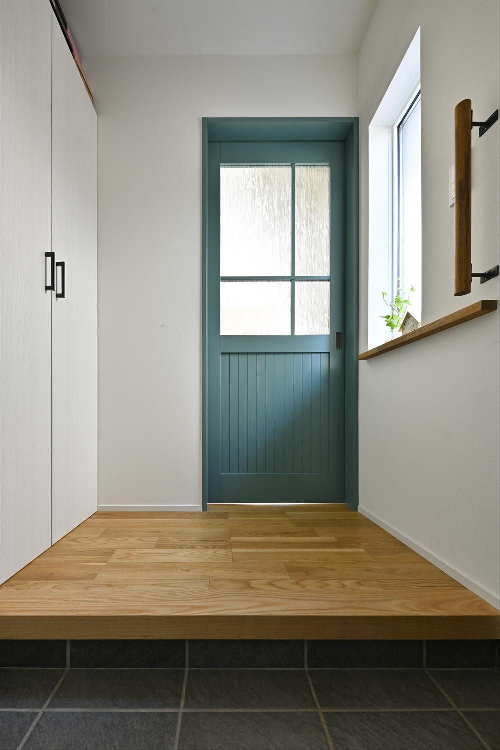 玄関を開けるとすぐに目に入るダイニングへ続く扉はデザインと色にこだわった。玄関は框の向きを変えて広いスペースを確保。壁一面の大きな収納で、2世帯6人分の靴がスッキル収まるように