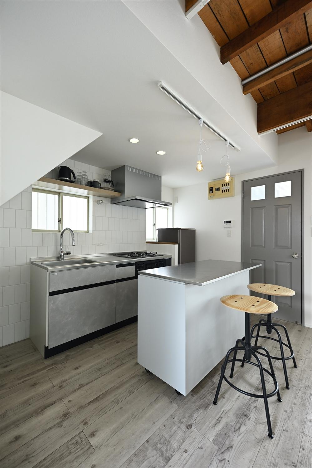 シンプルな壁付けキッチンの後ろにあるカウンターは移動式。使わないときは壁際に寄せたり、簡易バーとしても活用できる