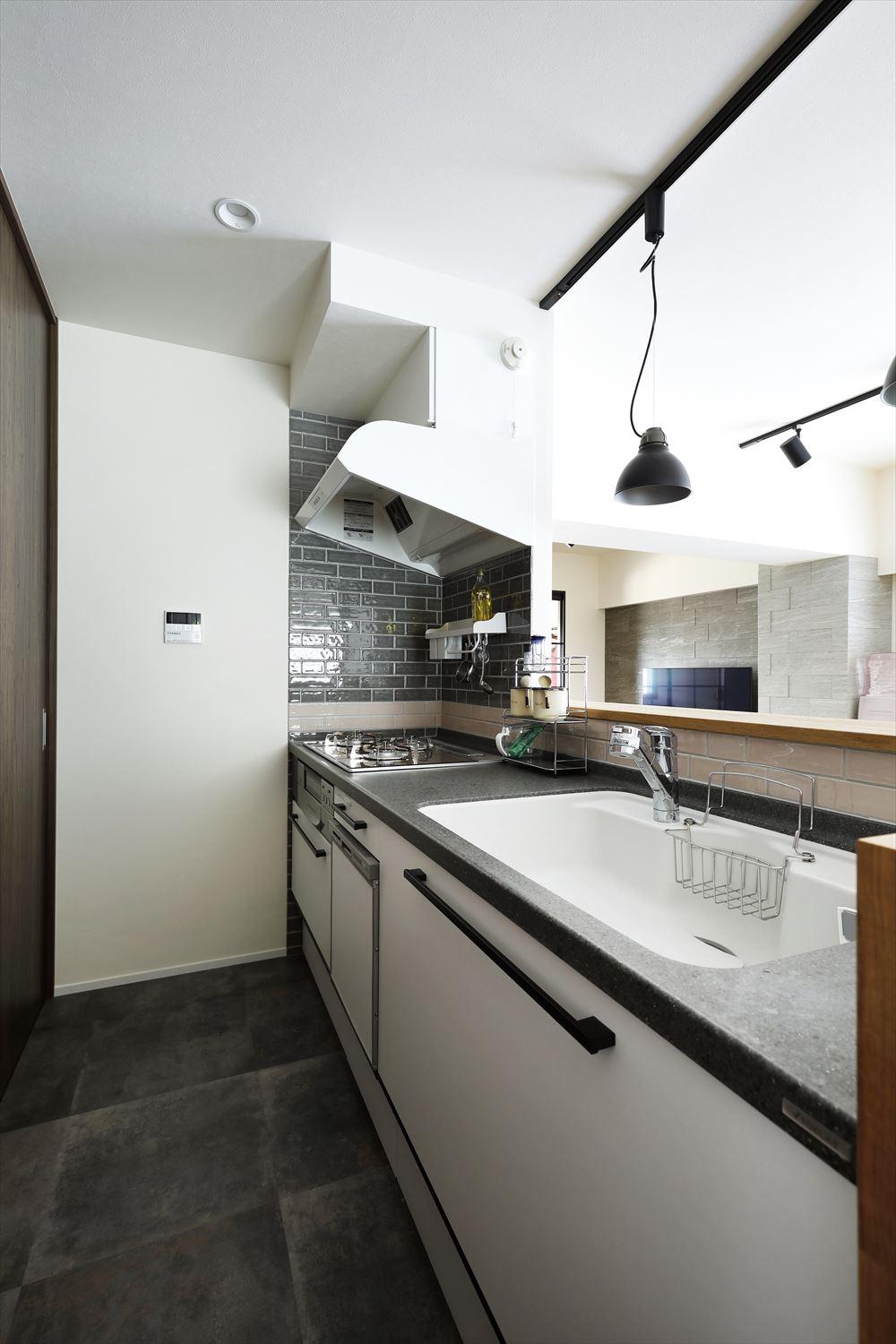 白を基調にしたキッチン。換気扇は白を選び壁と馴染むように。カウンターの立ち上がりの高さにベージュのタイルを、コンロ廻りはその上に深いグリーンのタイルを貼ってツートンに。細かいところにこだわりを感じられる。