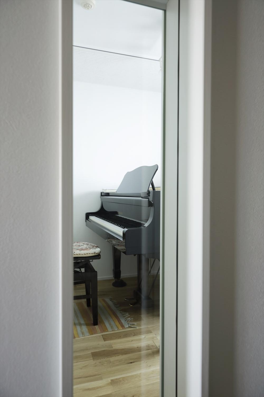 玄関ホール側のFIX窓から覗いた防音室内。それぞれの時間を過ごしていても、室内窓でお互いの気配を確認できる