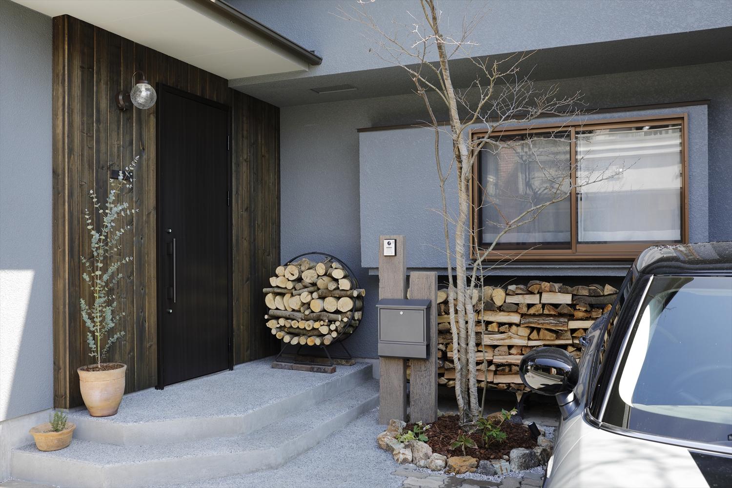玄関を1階に移動したことで2台分の駐車スペースが確保でき、外階段があった場所を活用してバイク置き場も実現。シンボルツリーなどは移植して再利用したもの。薪棚も素敵なアクセントに。庭側にはウッドデッキや薪割りコーナーを設け、自然に親しむ暮らしを叶えた