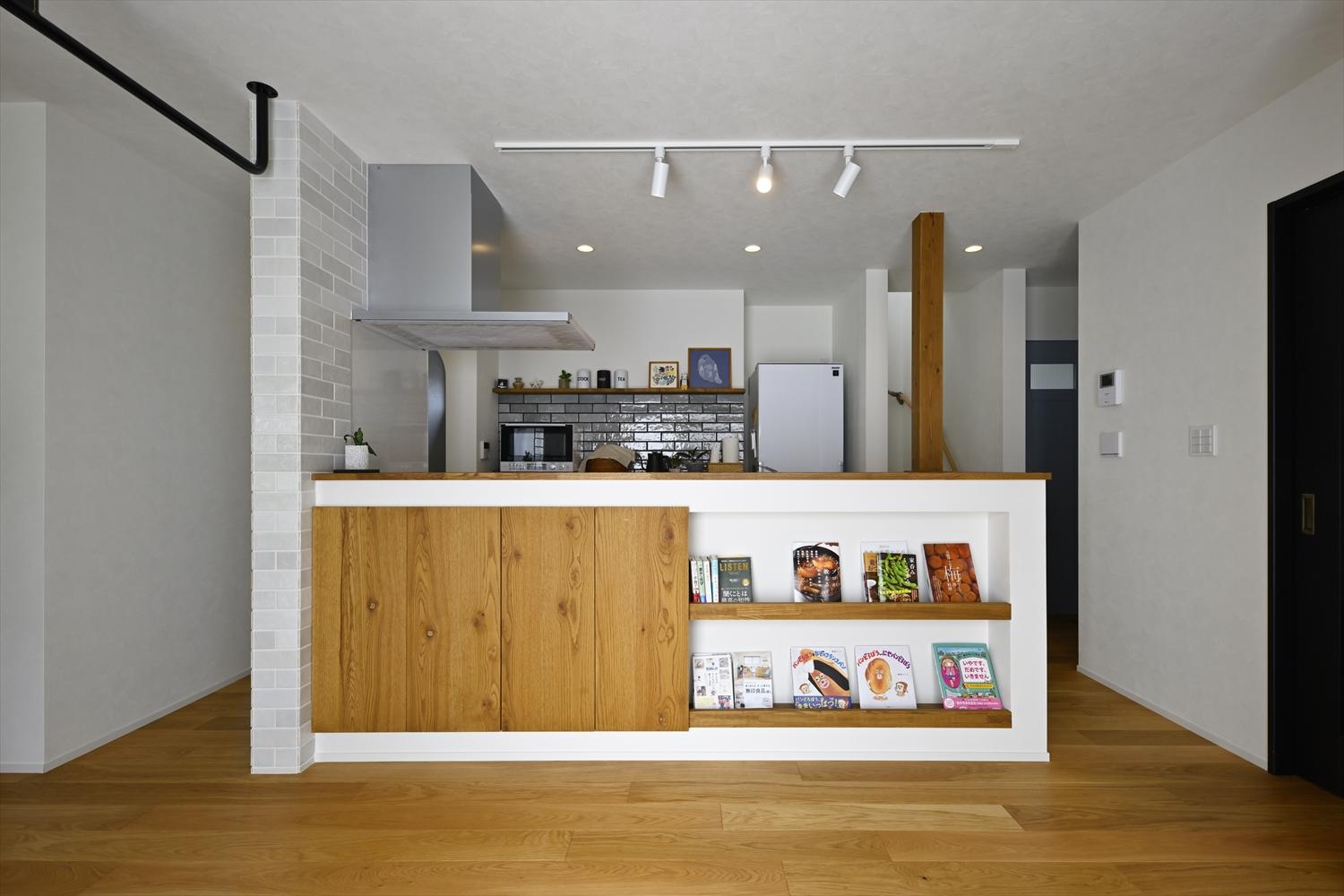 対面キッチンのカウンターにはマガジンラックや収納を造作。ダイニング・リビング周りのものもスッキリ片付く。サイドや背面の壁には濃淡が異なるグレーのタイルを採用してニュアンスのある空間に