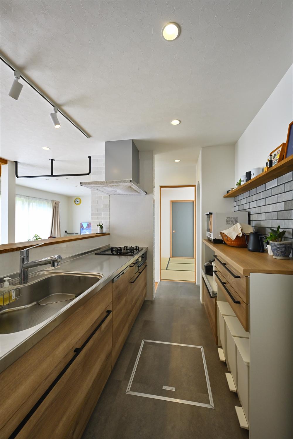 リビング・ダイニングの床材と色味を合わせた木目の面材が特徴的なキッチン。フロアの中央にあって1階全体が見渡せる。キッチンの裏には大容量のパントリーも。