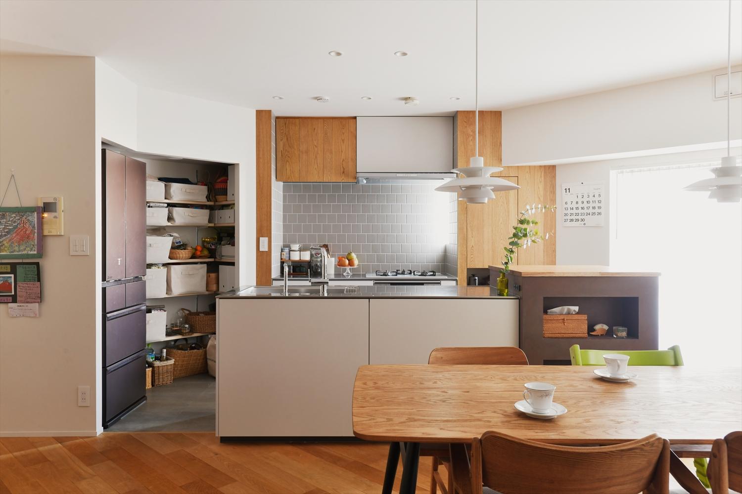 省スペースで回遊できるⅡ型キッチンを採用。背面にはグレーのタイルをあしらい、優しい雰囲気に。錆色のVALペイントで仕上げた家電収納がアクセントとなっている。