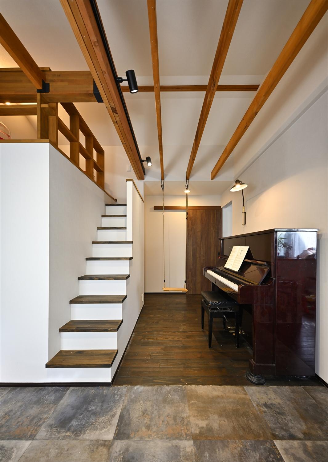 リビングの隣にお子さんたちの遊び場を実現。ピアノスペースには天井根太を活用してブランコを設置。バルコニーのある南側（写真手前）は味わいのある石目のフロアタイルを敷いてインナーテラス風に。