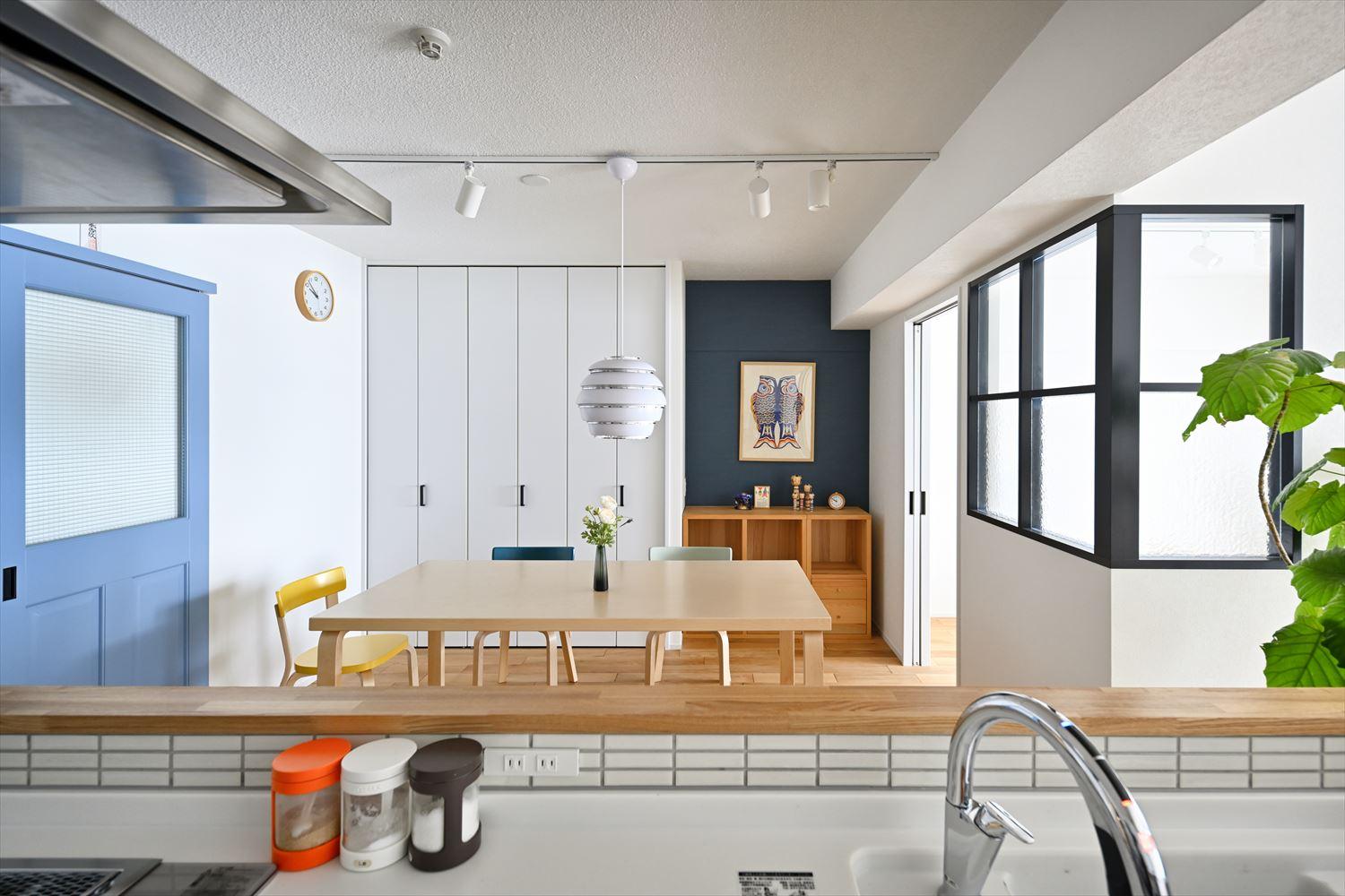 キッチンからみたダイニングと子ども室。白と明るい木目をベースにしたシンプルナチュラルな空間に廊下へつながる明るいブルーの建具がアクセントに。正面壁の一部に貼った深い色味のアクセントクロスで奥行きを感じられる