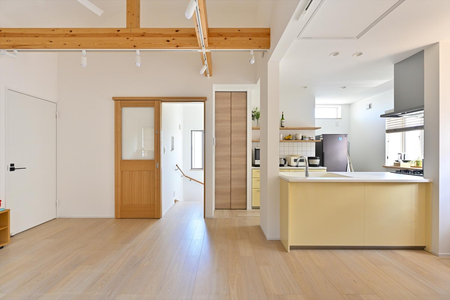 リビング入口の戸の大きなガラスが光を通して、空間を明るく開放的に。左手のドアの向こうは洗濯機＋洗面室。キッチン脇には大容量の収納を設置。