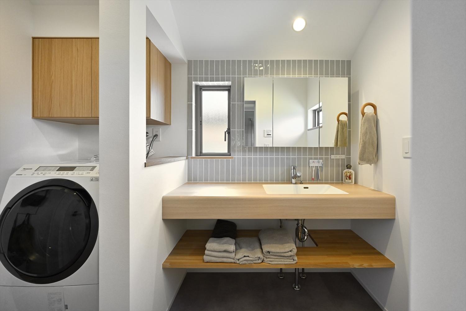 木目調の洗面カウンターと壁面のタイル貼りがやさしい洗面室。洗濯機のさらに左にウォークインクローゼットがあり、効率的な着替え・お洗濯の動線になっている。