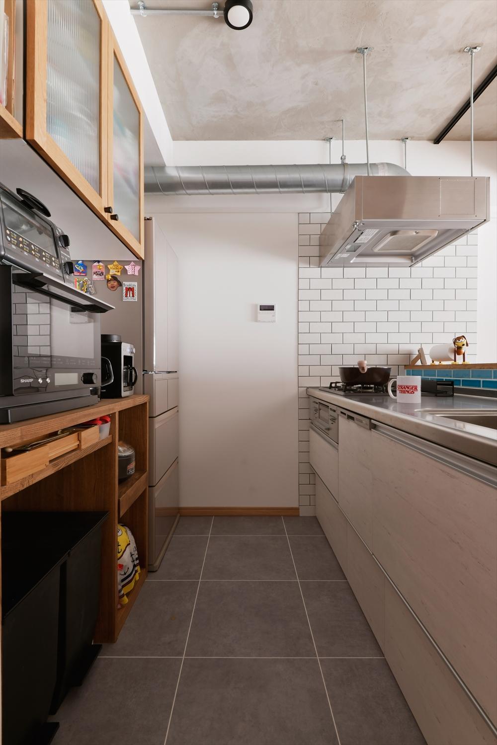 キッチン部分の床はフロアタイルに。木質の背面カウンターや壁面のタイル、駆体現し風天井などの異素材ミックスで、クールな中にも温かみのある雰囲気に。