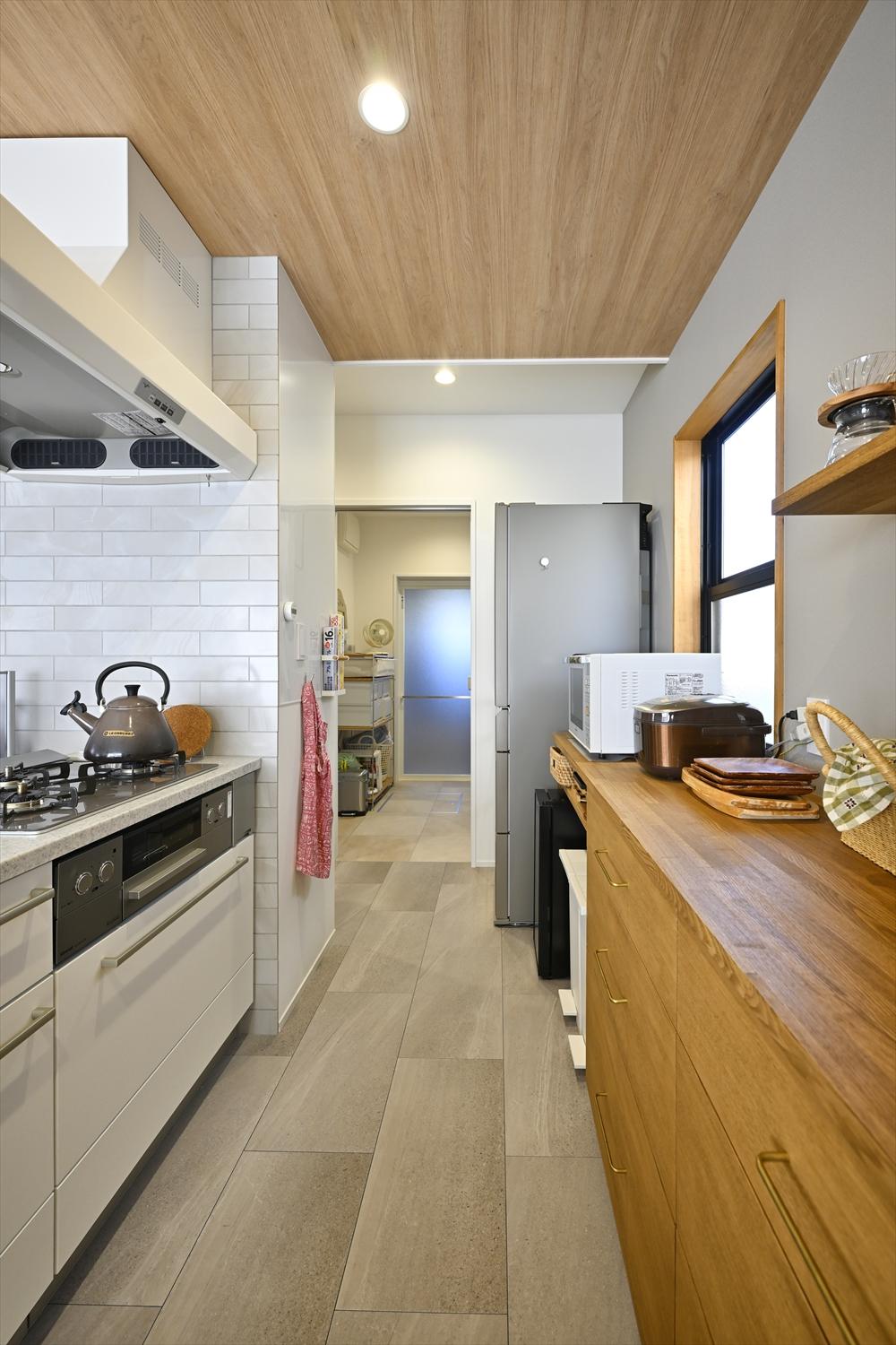 キッチン天井は木目調とし、背面の造作カウンターとともに自然な温もりを演出。写真奥の脱衣室兼ランドリールームにも直結させ、家事動線を短縮。