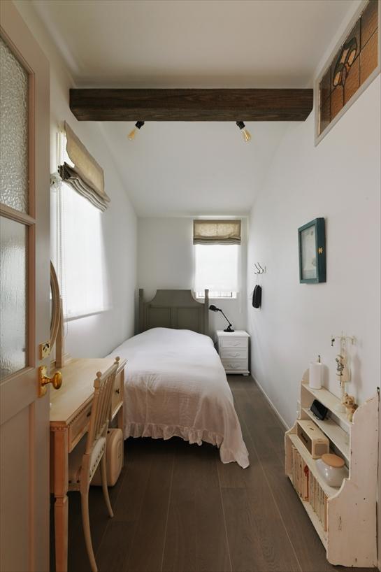 もともと納戸だった場所を妻の寝室にリフォームしました。奥に細長く、天井も高いため、一部を勾配天井にして見せ梁を加えることで、屋根裏部屋のようなあたたかみをプラスしています。廊下側の欄間にはステンドグラスを入れ、開口部はアイアン格子付きの上げ下げ窓に変更しました。