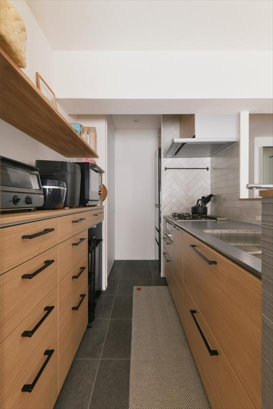 独立型だったキッチンは、LDと一体感のあるオープンな対面式に。背面に収納をたっぷり設け、奥には冷蔵庫を置けるパントリースペースも確保しました。カウンター周りにはシックなグレーのタイル、コンロ脇にはヘリンボーン柄の白いタイルを採用。インテリアとしても見応えのあるキッチンになっています。