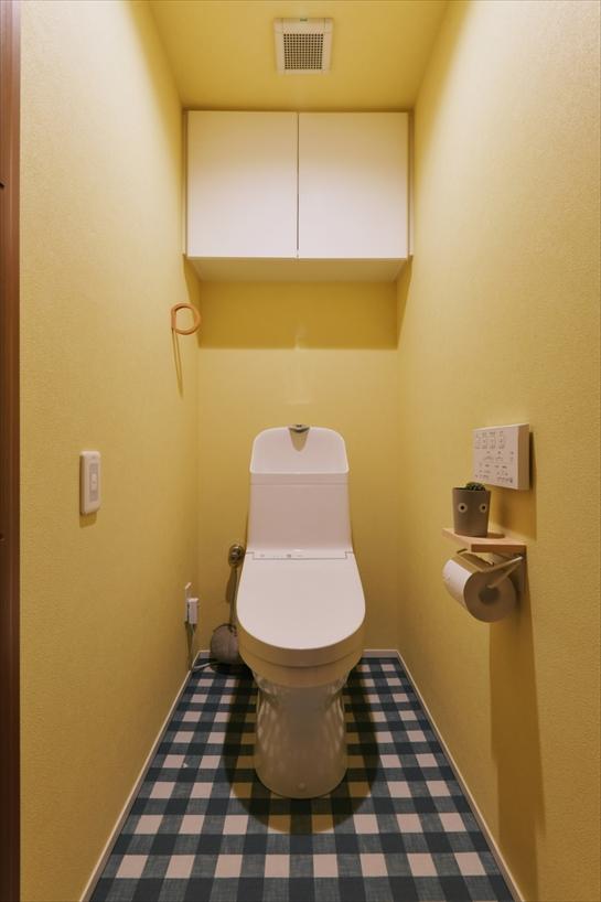 やわらかなイエローの壁に包まれた、明るく心地よいトイレ空間。チェック柄の床がアクセントとなり、シンプルな中にも遊び心を感じられる仕上がりです。収納もすっきりと収まり、使い勝手にも配慮しています。