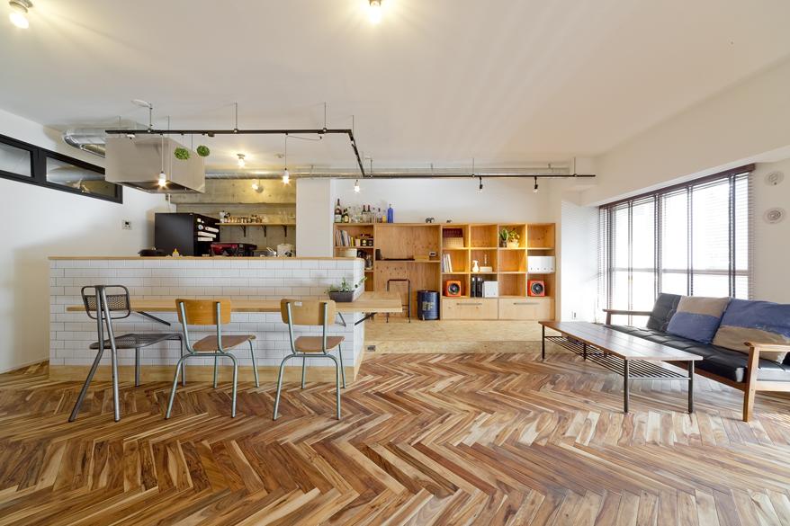 マンションならではの広々したリビング。無垢材（ミモザ）を使用したヘリンボーンの床と、キッチンOSB合板を使用し、素材をかえることでわざとつけた段差が空間にアクセントとなりました。