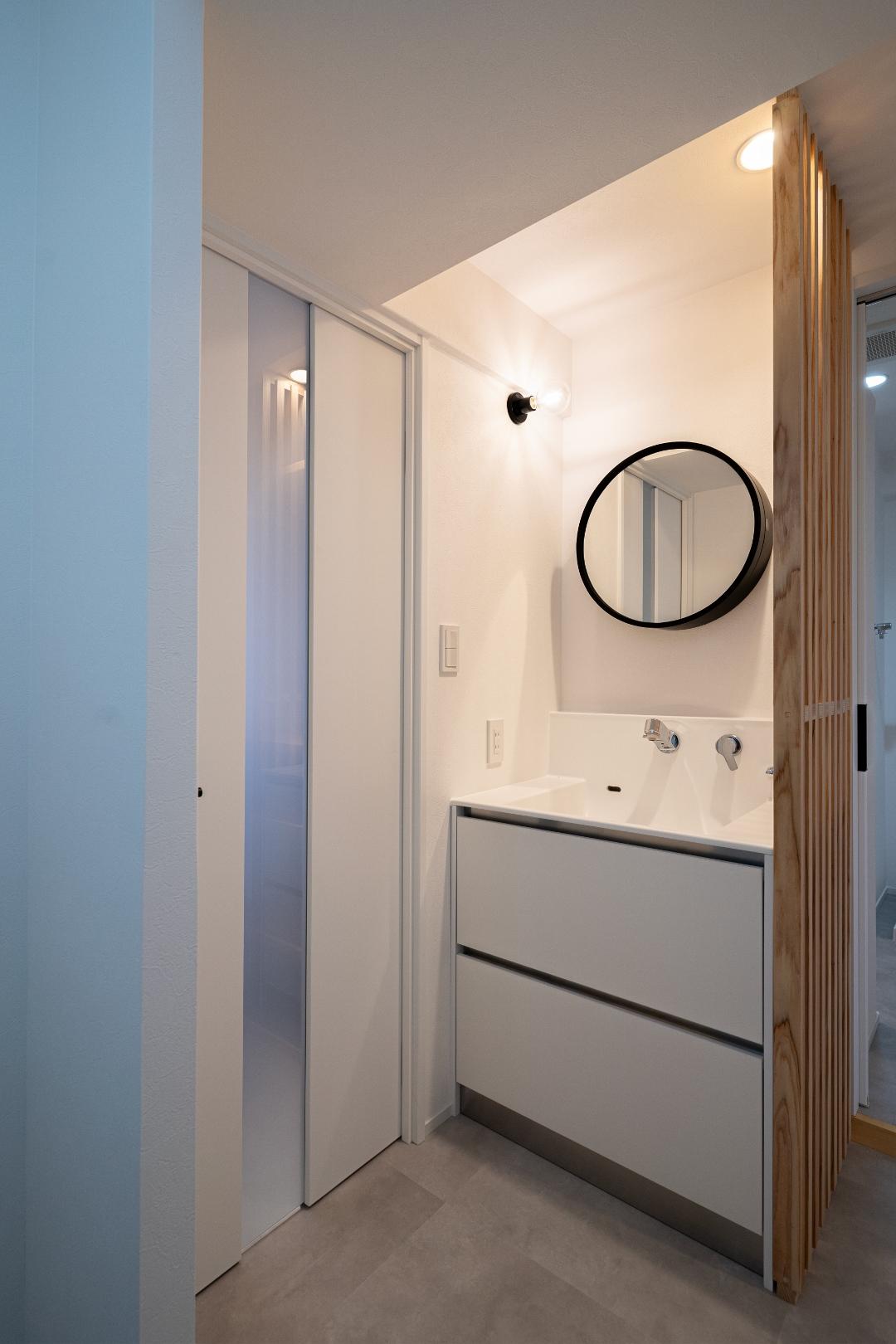 洗面台横の木材の格子は、玄関から目隠しする役割の他、インテリアに和のアクセントを添えるポイントにもなっています。
ラウンドミラーがモダンな造作風の洗面台は、既製のものを採用。コストバランスをとりつつ、インテリアと調和するようデザインを選定しました。