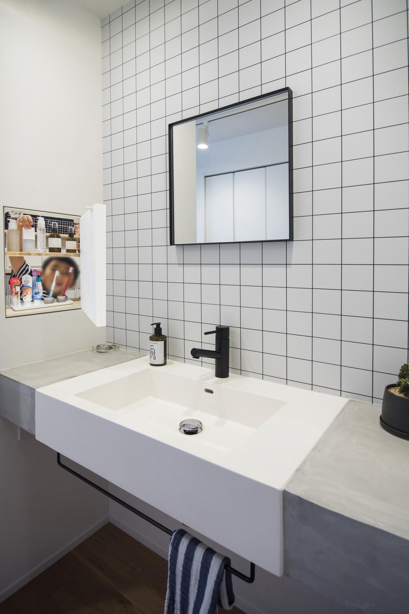 モダンで瀟洒な雰囲気を醸し出す洗面化粧台です。
洗面ボウルの両サイドには、モルタルを使用してちょっとした荷物を置けるスペースを作り、前面の壁紙は、防カビ機能のあるタイルを採用。サイドの収納は隠し扉になっていて、日用品は取り出しやすくて便利な上、生活感も出さずにホテルライクな気分を味わえます。