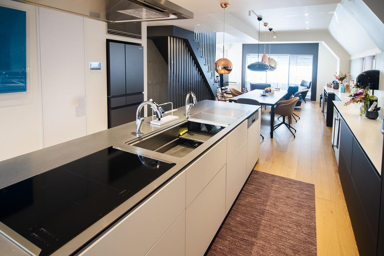 上部の収納は使いづらいので、収納は全て下に設けたというキッチン。キッチンの天板には上質感のある薄いステンレスを採用し、天板が浮いて見えるようなデザインに。天板の下に2cmの黒い板を挟み、向かいのカウンター側にも座りやすいよう設計しています。