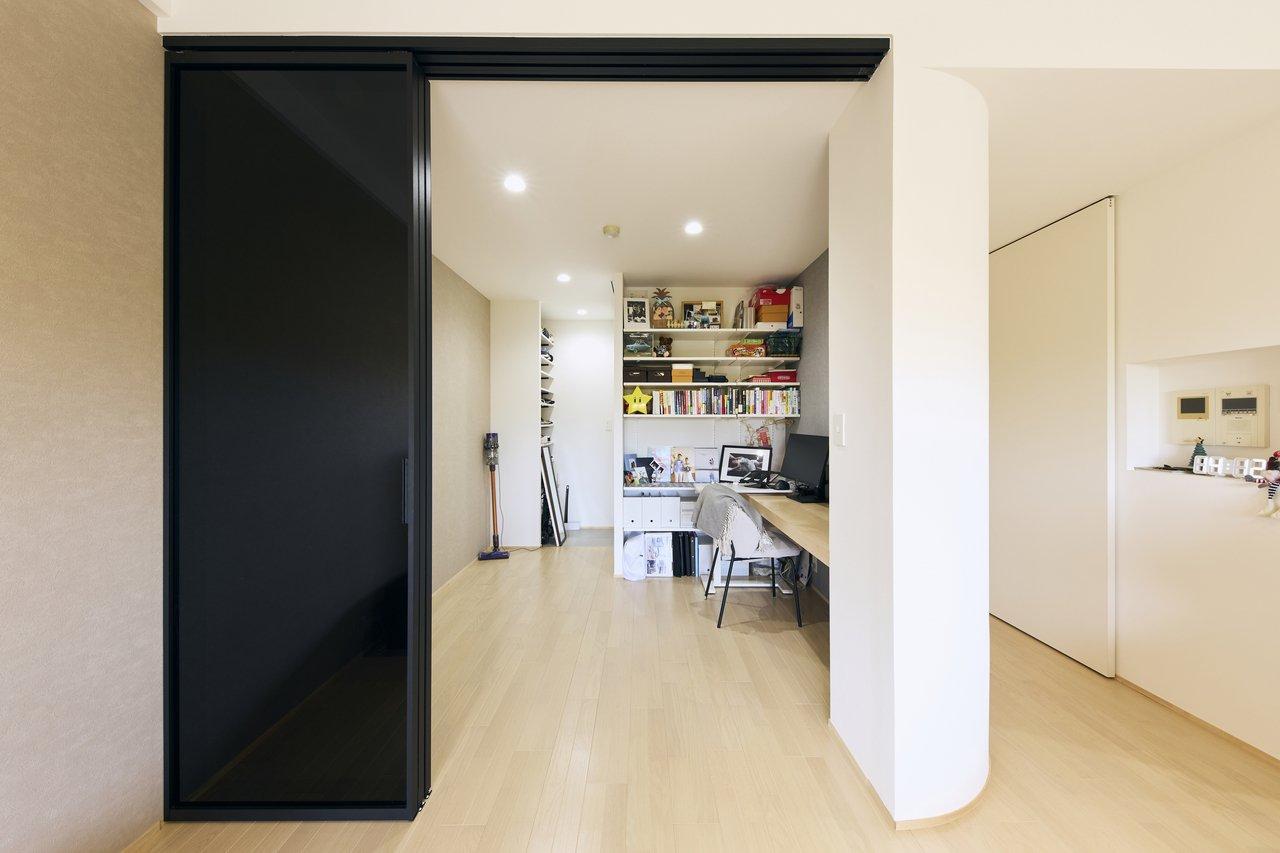 ガラス引き戸でリビングとつながる約5.4帖のサービスルーム（納戸）は、在宅でお仕事をされる奥様のワークスペースです。椅子を並べてお子さんと一緒に勉強ができる広さのデスクに設計しました。奥は可動棚を設置したシューズインクローゼットになっており、白い引き戸を開けると玄関と繋がります。