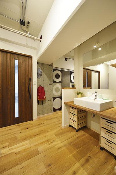 無駄に大きい廊下・ホールに洗面スペースを移設した事で、１日を通してストレスを感じさせず、使いやすくなった。造作した洗面は、木の天板でシンプルに。洗面下は造作せず、既製品の収納家具を入れられるように計画。コストダウンとフレキシブルな収納を実現した。