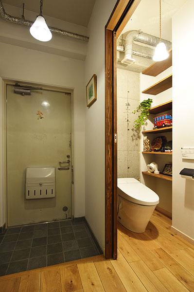 正面の躯体の壁がアクセントとなっているトイレ。子供部屋と同様に上吊の建具を採用。床が完全にフラットになり、誰でも出入りしやすい。また、洗面スペースを廊下に出した分、広くなった脱衣室を上手く活用して、トイレに棚や手洗スペースを造作し、より快適な空間へ。