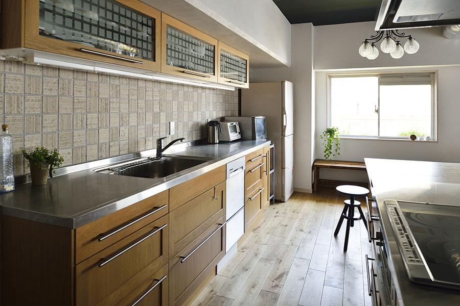 ゆったりとした広さのキッチンは、施主支給。２列型でサイズも大きく存在感はあるが木の扉が家具のように空間に馴染む。キッチンのシンク側に貼ったランダムに貼ったタイルの素材感が珪藻土の壁に馴染みつつ、LDK空間にほどよいアクセントとなっています。