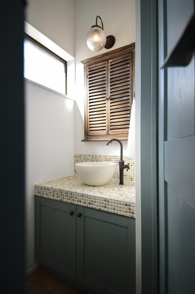 レトロなデザインを織り交ぜたトイレ手洗いコーナーです。お鉢のような手洗いボウルに鶴首の水栓。水彩のようなモザイクタイルにグリーンの建具がとても良く似合っています。鏡には木の温かみを感じる扉窓を造作してアンティークなニュアンスもプラス！