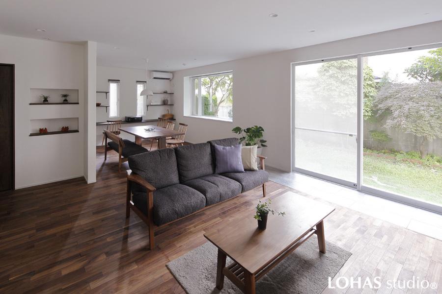 庭を広々と見渡せる心地よいLDです。渋みのある茶色の床は無垢ウォールナット材。壁には漆喰を施工して柔らかな雰囲気を出しました。縦長の窓に似せてニッチを造り世界観を統一。