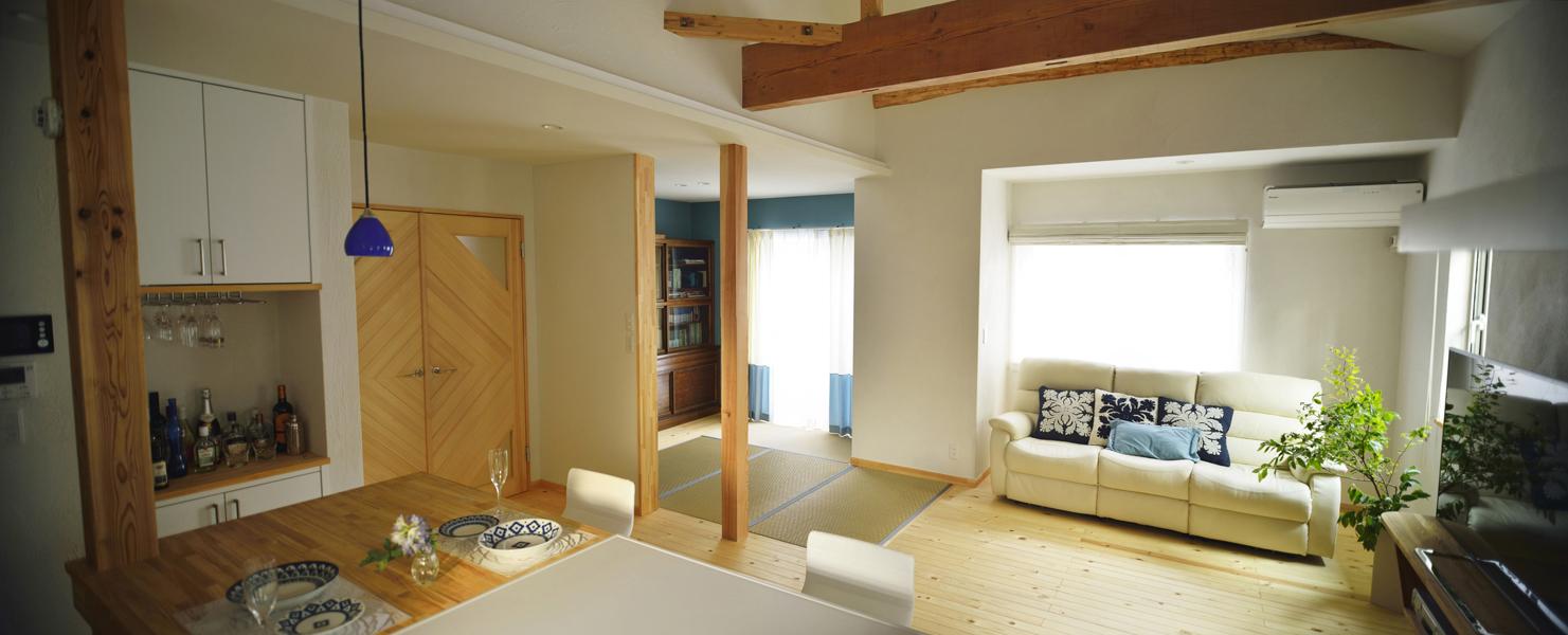 天井を抜いて造った吹き抜けのあるホール状のリビングです。扉の奥は階段で回遊性の高い動線を実現。あらわしになった柱や梁で温もり感あるデザインです。天井にはシーリングファンを設置して広い室内を空気循環します。