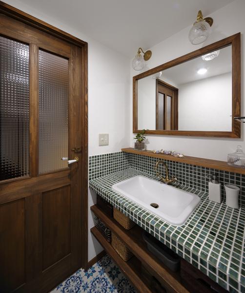 レトロモダンな風合いの洗面室です。グリーンのタイルを使った可愛らしい洗面台はお好みに合わせた造作品。左手の扉も同様でドアノブやガラスなどパーツごとにお気に入りを反映したLOHAS studioオリジナルです。洗面台の下は便利な収納スペース。