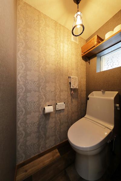 植物柄のクロスに裸電球 オレンジ色の照明光。昭和ロマンを彷彿とさせるデザインのトイレです。個性的な小窓は50年前の竣工当時のまま。洗練されたアイテムを合わせてご祖母様の面影を残し とある「時代」の空気を創りました。