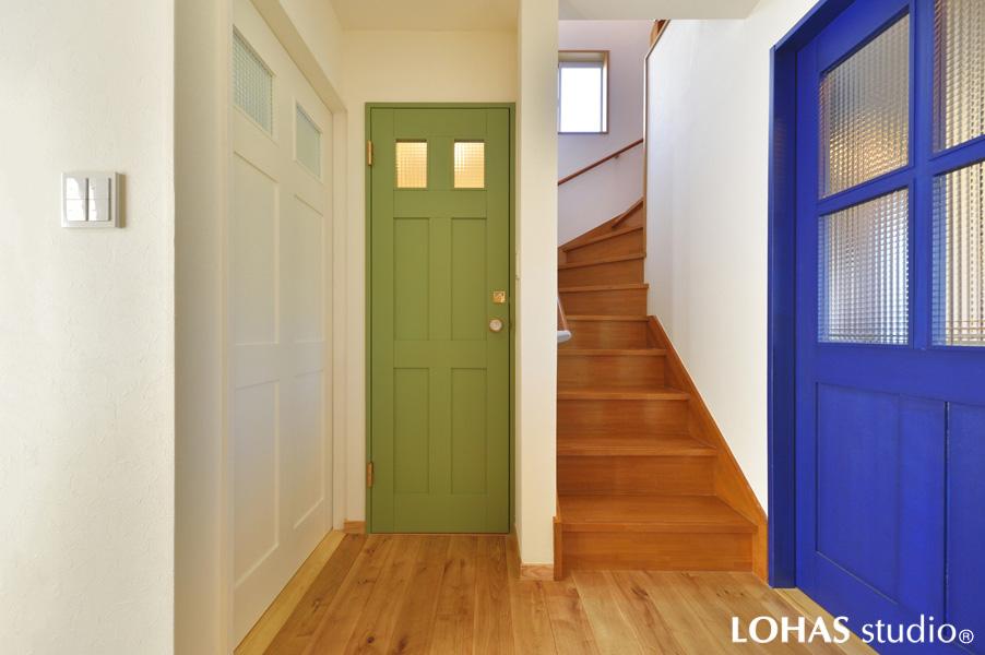 カラフルな扉が印象的な玄関ホールです。「入ってびっくりする家にしたい」のご要望で生まれた「不思議」で「楽しい」景観です。行先の違う3つの扉はどれも無垢材で造作したオリジナル建具で色選びにもこだわりました。扉の先の室内とも素敵に馴染んでいる洗練された空間です。