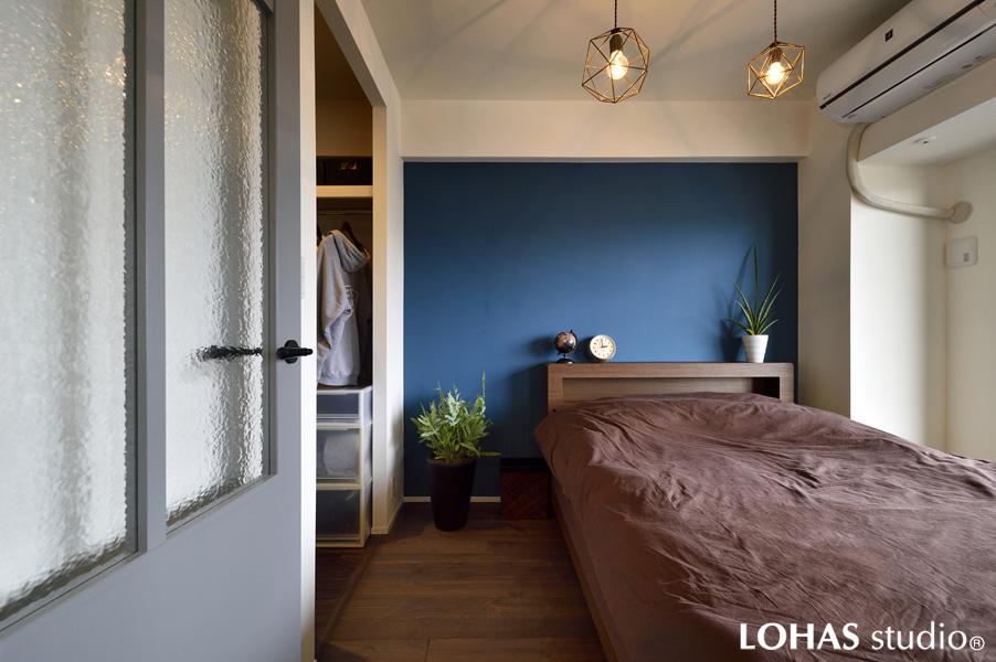 壁一面にブルーを塗装したカジュアルモダンな寝室です。間仕切りにガラス入りの造作窓を設けて開放感をプラス。実寸より大きく感じる伸びやかな室内です。足元は遮音 マットの上に触り心地の良い無垢材を施工。