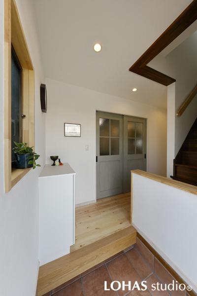 木の風合いを感じる親しみやすい玄関です。擦れ感のあるクラシカルな土間はイタリア製のテラコッタ調タイル。階段側の腰壁がプライベート感を強調しています。