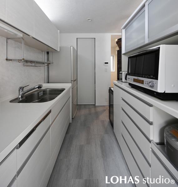 白基調のスタイリッシュなキッチンです。床には石目調タイル、壁には珪藻土を施工するなど異なる素材で白を彩りました。上下たっぷりの収納のほか奥にはパントリーも新設。