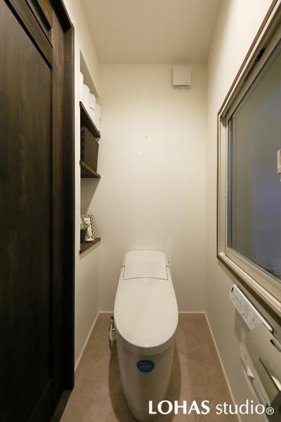 色を抑えたストイックな印象の洗練されたトイレです。ニッチを使って備品の置けるオープン棚を造作しました。タンクレスで室内は広々。床は汚れに強いクッションフロアをご採用です。