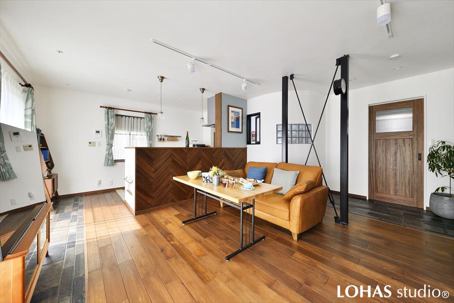 無垢フローリングにタイルを組み合わせた個性的なLDKです。窓際にタイルを施工することでインナーテラスのような装いになりました。制約上動かせない鉄骨ブレースには、両面時計を付けてインテリアの一部としています。