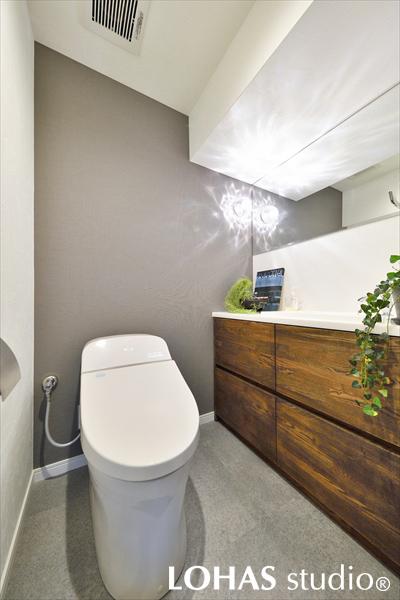 水のゆらぎを思わせる照明が印象的なトイレです。グレーのアクセントクロスでシンプルにまとめ、収納力のある造作洗面台を施工しました。