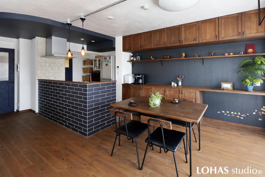 モノトーンカラー＋無垢材で落ち着いた印象を与えるLDKです。漆喰で塗られた天井には、武骨なアイアン素材でアクセントを加えて男前なインテリアに。排気ダクトの関係でやむなく下げる必要のあったキッチン上部は、あえてアールのデザインを施すことでお洒落度がアップしています。