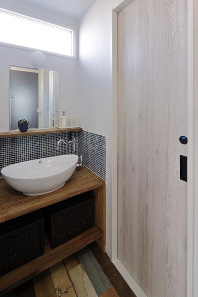 キッチンから繋がるスタイリッシュな洗面室です。ぽってりした洗面ボウルにタイルが美しく映えています。白い引き戸はトイレの扉。