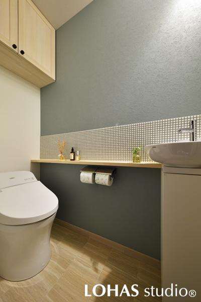 壁の一面をブルーグレーにしたトイレです。洗面ボウルで濡れがちな部分にのみタイルを施工。防カビ性能のあるカラー目地を使うことで、白い小花が咲き乱れたような可愛らしい仕上がりとなりました。